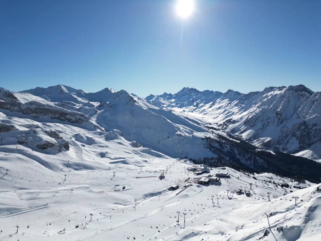 Schneebedeckte Berge unter einem klaren blauen Himmel, über dem die Sonne hell scheint.