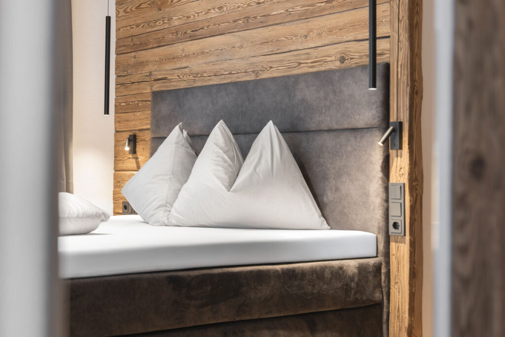 Ein modernes Bett mit weißen Kissen und einem grauen Kopfteil vor einer Holzwand.